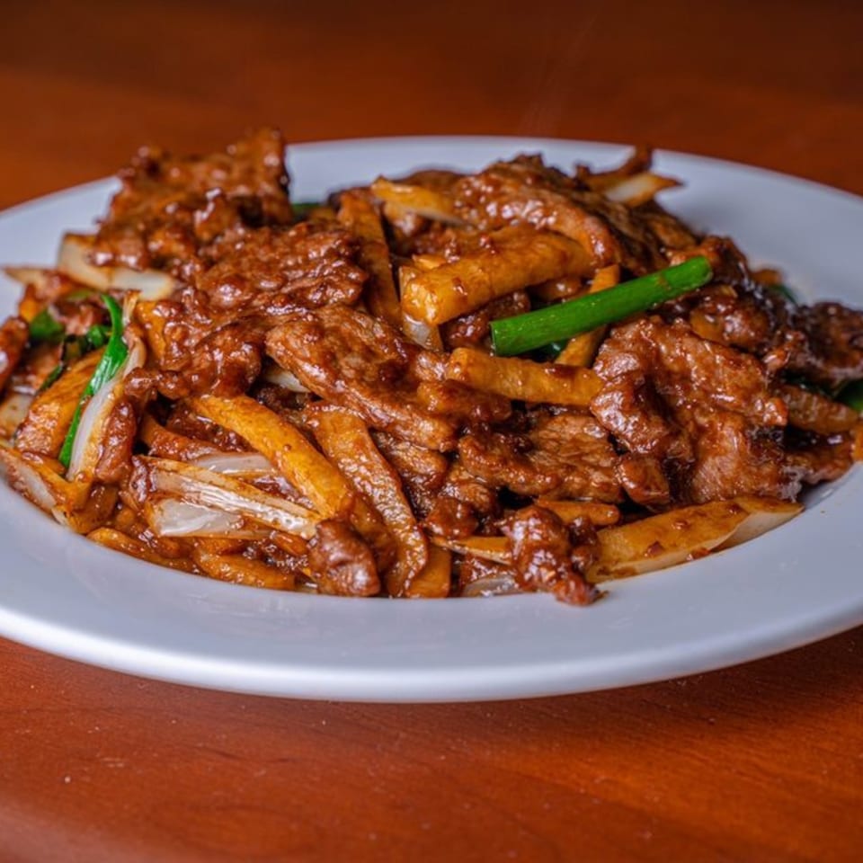 Modern Fusion's Asian-fusion dish with beef, onions, and green scallions on a white plate.