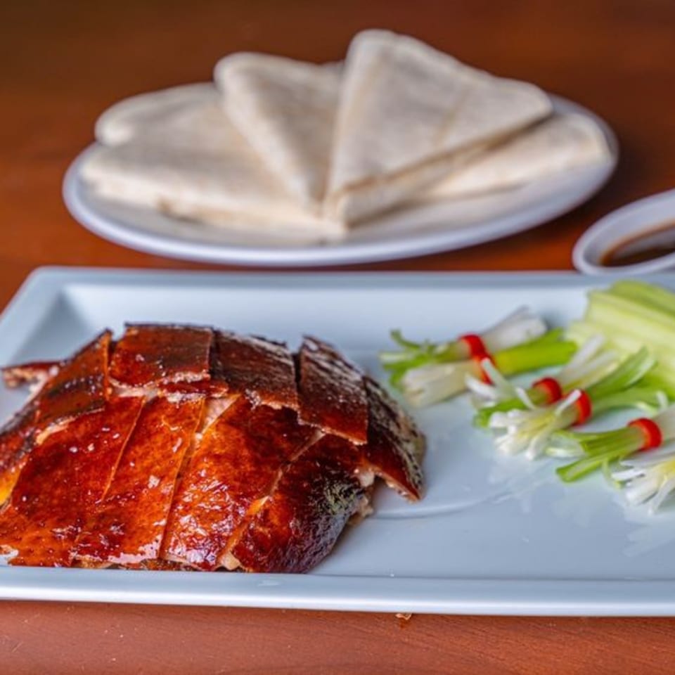 Sliced Peking duck with crispy skin, scallions, and pancakes on white plates.